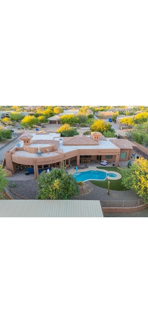 A large house with a swimming pool, surrounded by trees and a well-maintained lawn.