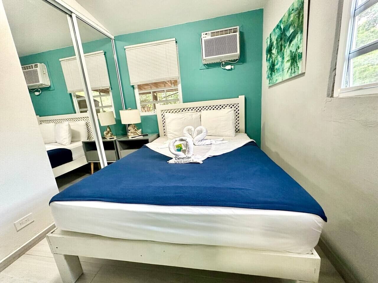 Una cama con una colcha azul y almohadas blancas, un cabecero blanco, y un felpudo con un diseño de cisne.