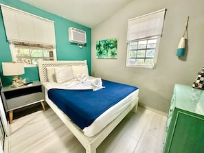 A bedroom with a bed, bedside table, lamp, air conditioning unit, and a window with blinds. - Villa 11 Flamenco Beachfront Villa (Flamenco)