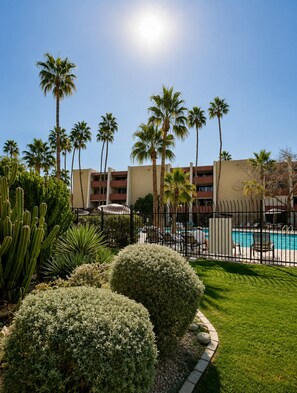Area piscina hotel con palme, piscina recintata e un edificio con numerosi balconi.