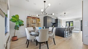 Una cocina moderna con una isla central, una zona de comedor con una mesa redonda y sillas, y una planta grande en maceta.