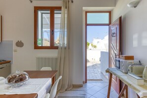 A kitchen with a dining table, a radiator, a window with curtains, and a view of the outside. - Apartment 'Casa Buongiorno Salento' with Private Terrace, Wi-Fi and Air Conditioning (Patù)