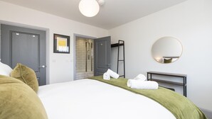 Et hotelværelse med en seng, brusebad, et spejl og et indrammet kunstværk på væggen.