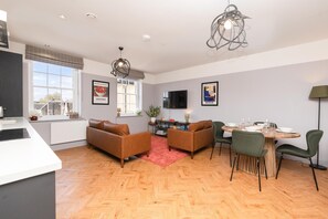 Un salon moderne avec une cheminée, un coin repas avec une table et des chaises en bois, et une cuisine avec un plan de travail blanc.