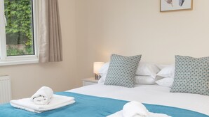 Cama bem arrumada com roupa de cama azul, duas almofadas com padrão geométrico e uma janela com cortinas.