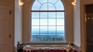 A bathroom with a large arched window, a bathtub, and a view of a cityscape. - Mountain Estate | Pickleball, Hot Tub, Game Room (Port Angeles)