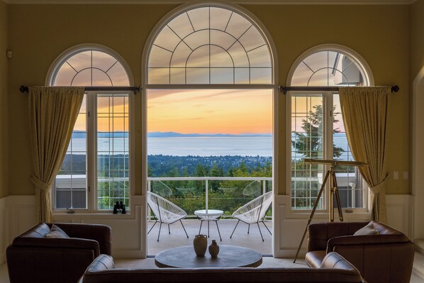 A room with a balcony, two white chairs, a round table, and a sofa.