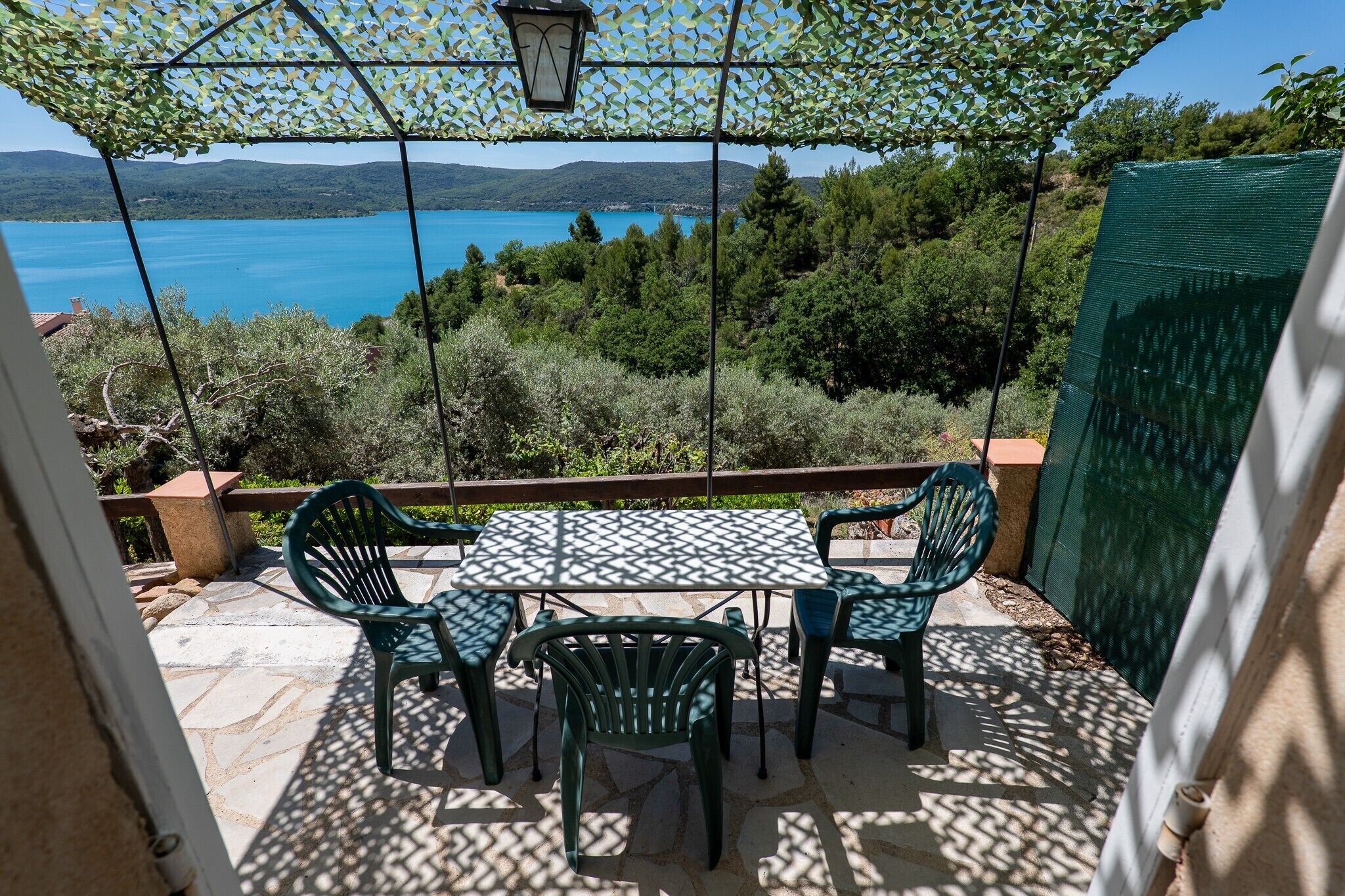 A patio with a table and chairs, overlooking a lake and hills.