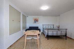 A room with a bed, a table with chairs, a sofa, and a painting on the wall.