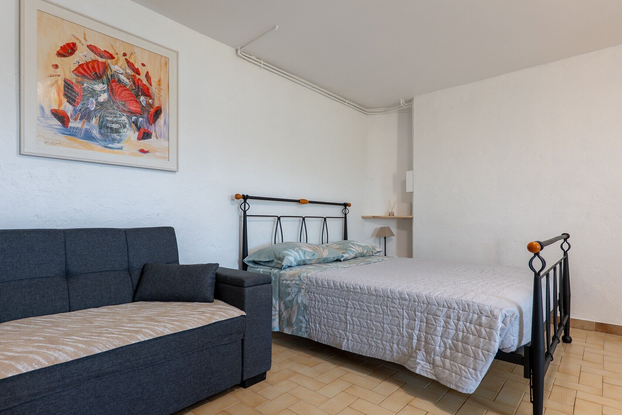 A room with a bed, a sofa, a painting, and a lamp.