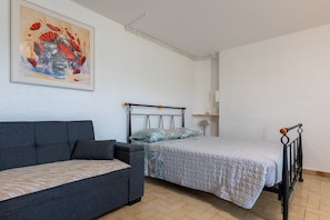 A room with a bed, a sofa, a painting, and a lamp.
