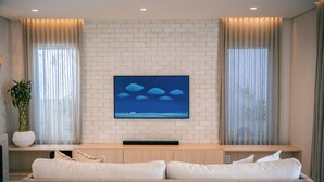 Una sala de estar moderna con un televisor de pantalla plana montado en una pared de ladrillo, un sofá con cojines y una planta en maceta.
