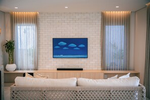 Ein modernes Wohnzimmer mit einem Flachbildfernseher an einer Ziegelwand, einer Couch mit Kissen und einer Topfpflanze.