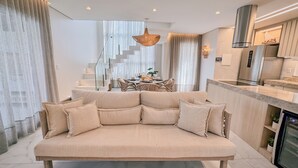Una sala de estar moderna con sofá, comedor, escalera, cocina y una lámpara colgante.