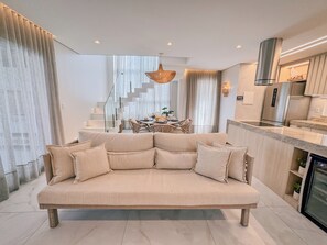 Ein modernes Wohnzimmer mit Sofa, Essbereich, Treppe, Küche und einer Pendelleuchte.
