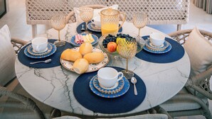 Comedor con una mesa redonda dispuesta para el desayuno, una lámpara colgante de mimbre y un banco blanco acolchado.