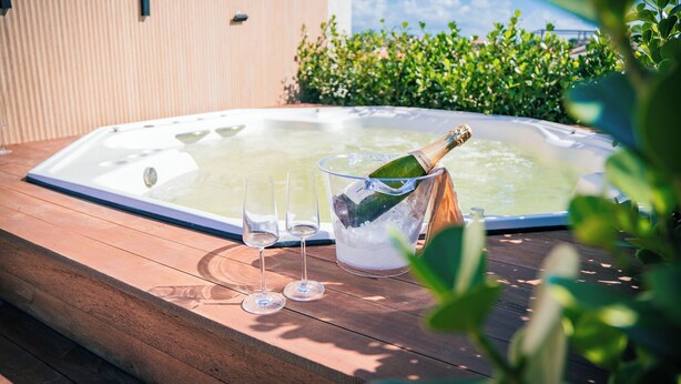 Un jacuzzi con dos copas y una botella de champán en una terraza de madera.