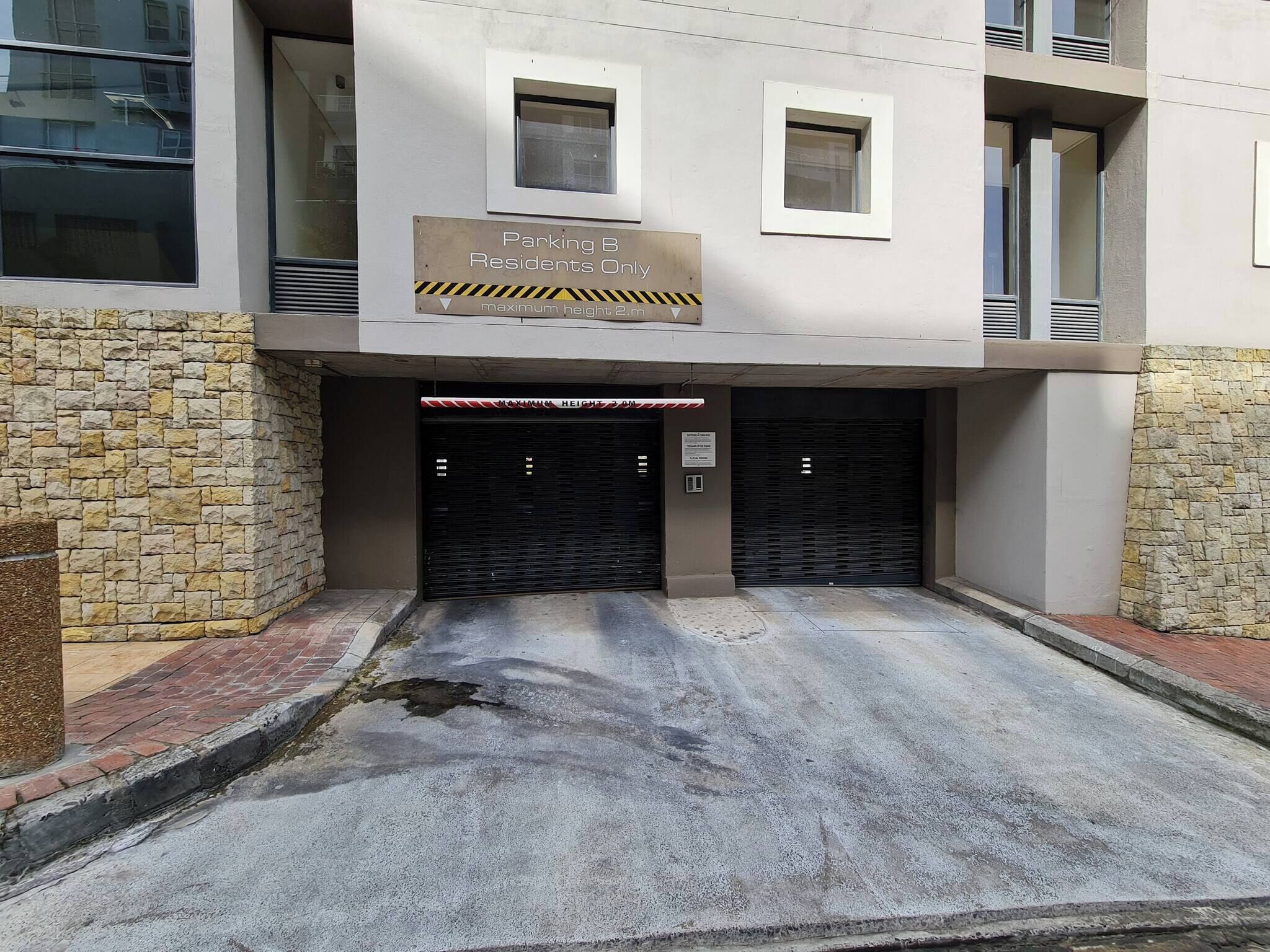 Entrada de edificio con un letrero que indica estacionamiento B solo para residentes y una altura máxima de 2,1m.