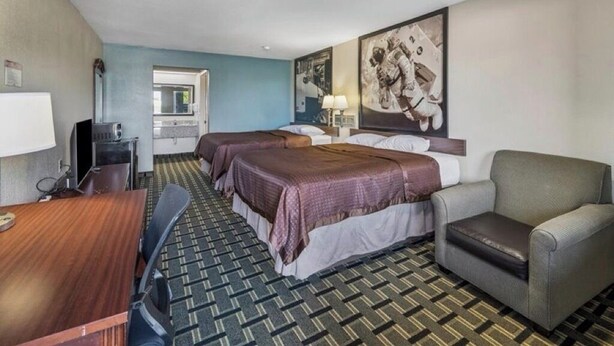 Habitación de hotel con dos camas, un escritorio, una silla, un televisor y un cartel grande en la pared.
