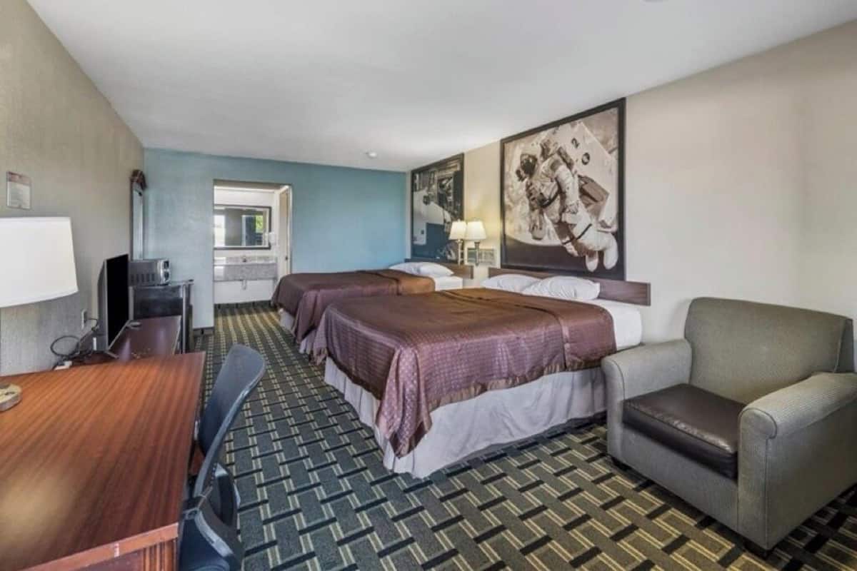 Habitación de hotel con dos camas, un escritorio, una silla, un televisor y un cartel grande en la pared.