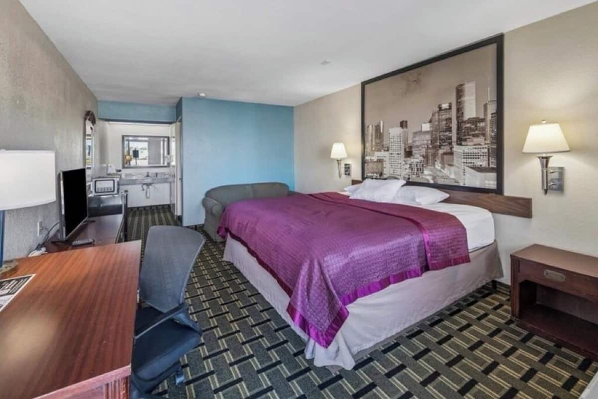 Habitación de hotel con cama, escritorio, silla, televisión y un cuadro con una vista urbana.