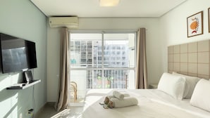 A hotel room with a bed, a TV, a window with curtains, and a view of buildings outside. - Home Bikers (São Paulo)