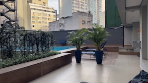 A rooftop pool area with lounge chairs, potted plants, and a view of surrounding buildings. - Home Bikers (São Paulo)