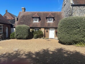 A traditional brick house with a tiled roof, two windows, and a white door.