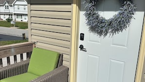 A white door with a wreath, a green doormat, and a wicker chair with a green cushion. - Nice 2-bedroom in charming Smithville near Lake. Onsite boat parking available. (Smithville)