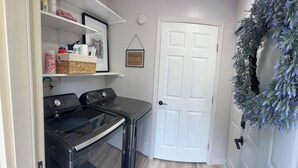A laundry area with a washing machine, dryer, and shelves with various items. - Nice 2-bedroom in charming Smithville near Lake. Onsite boat parking available. (Smithville)