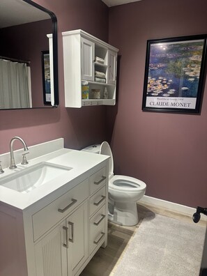 A bathroom with a white vanity, a sink, a toilet, a mirror, and a Claude Monet painting. - Nice 2-bedroom in charming Smithville near Lake. Onsite boat parking available. (Smithville)