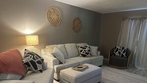 A living room with a grey sofa, ottoman, and armchair, a lamp, and decorative wall art. - Nice 2-bedroom in charming Smithville near Lake. Onsite boat parking available. (Smithville)