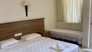Une chambre d’hôtel avec un lit double, une table de chevet, une lampe, une fenêtre avec des rideaux et un canapé.