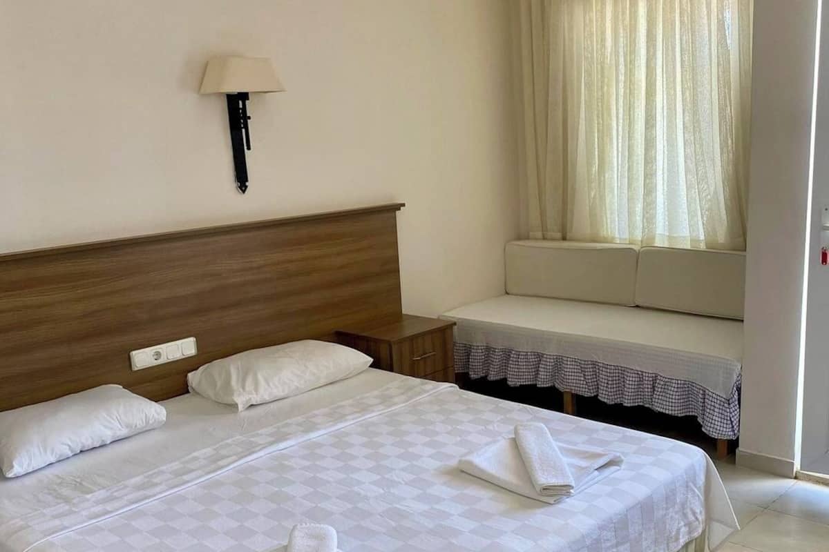 Habitación de hotel con una cama doble, una mesita de noche, una lámpara, una ventana con cortinas y un sofá.