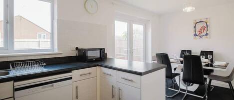 A modern kitchen with white cabinetry, a black countertop, and a dining area with a table and chairs.