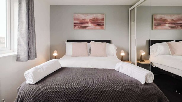 Une chambre d’hôtel comprenant un lit, deux tables de chevet avec des lampes, une fenêtre avec des rideaux et deux tableaux accrochés au mur.