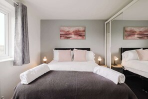 Ett hotellrum med en säng, två sängbord med lampor, ett fönster med gardiner och två tavlor som hänger på väggen.