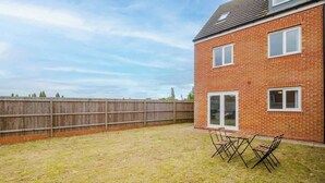 Une maison en briques avec un jardin clôturé, une table de patio et des chaises.