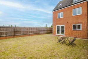 Ein Ziegelhaus mit einem eingezäunten Garten, einem Terrassentisch und Stühlen.