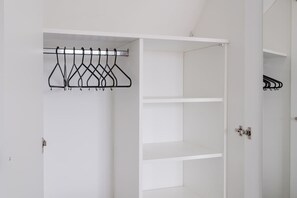 Een witte kast met een metalen kledingroede en open planken.