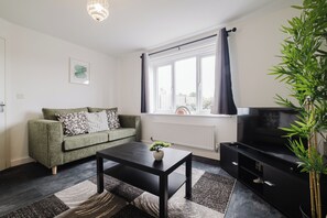 Ein Wohnzimmer mit einer Couch, einem Couchtisch, einer TV-Konsole und einem Fenster mit Vorhängen.