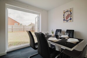 Ein Essbereich mit Tisch für zwei Personen, schwarzen Stühlen, einem Fenster mit Blick auf einen Hinterhof und einem an der Wand hängenden Bild von Chilischoten.