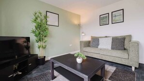 Un salon avec un canapé, une table basse, un téléviseur et une plante en pot.