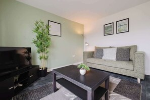 Ein Wohnzimmer mit einer Couch, einem Couchtisch, einem Fernseher und einer Topfpflanze.