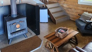 Ein Blockhaus-Interieur mit Holzofen, Treppe, Holzwand und einer Kandelaberleuchte.