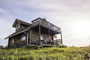 A wooden cabin with a balcony, a covered porch, and a small outdoor seating area. - COTC: Log Cabin Glamping (Castor)