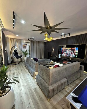 Ein modernes Wohnzimmer mit einem Ecksofa, einem Hängekorbstuhl, einem Flachbildfernseher und einem Deckenventilator.