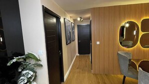 A modern interior with a wooden floor, a dining area with two chairs, a white vase with a plant, and a black door. - Attention By Ndifon (Abuja)