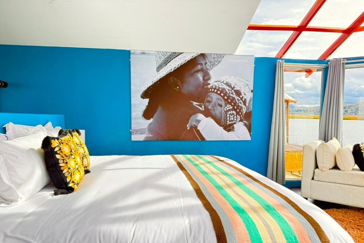 A hotel room with a bed, a sofa, a large window, and a framed picture on the wall.