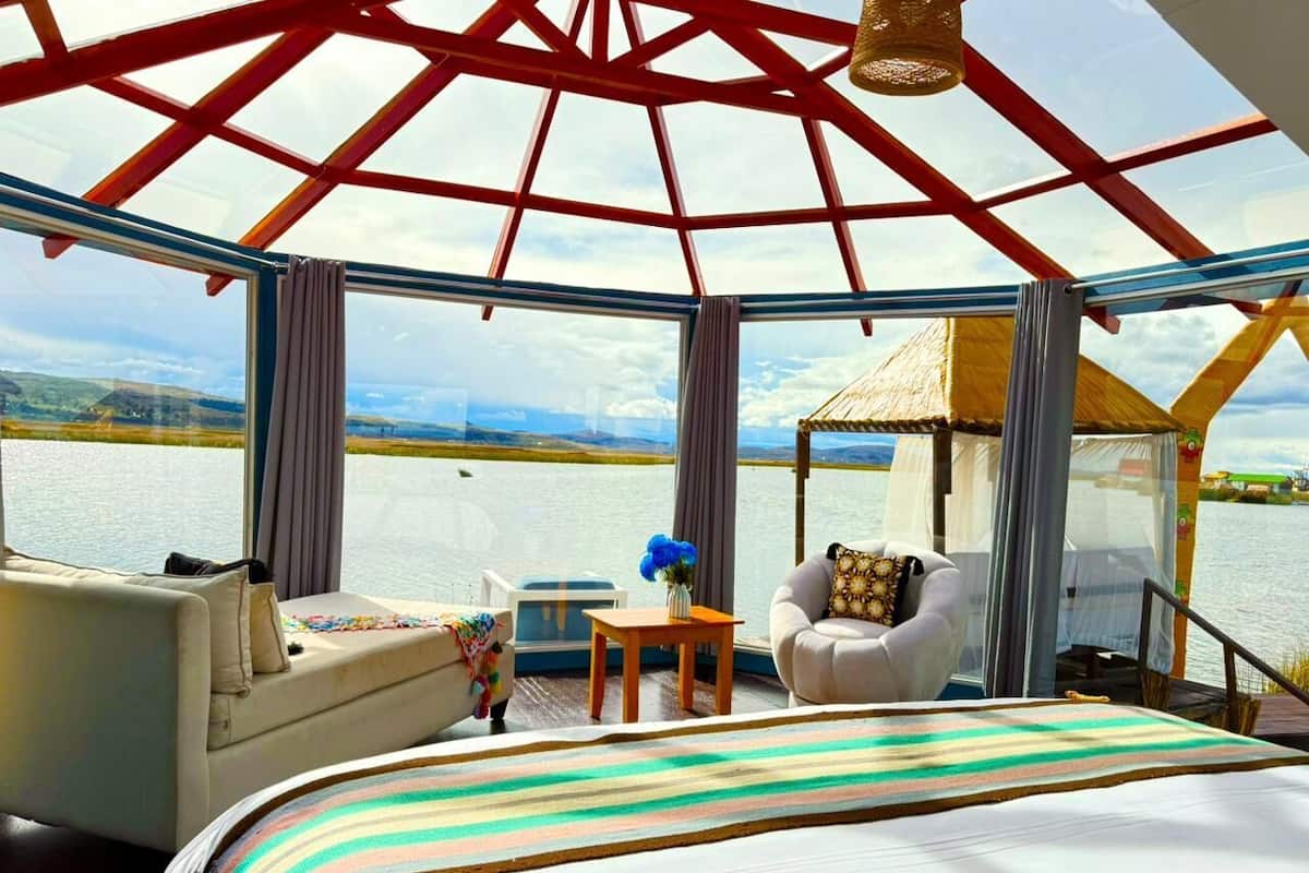 A room with a bed, two sofas, a small table, and a view of a body of water through large windows.